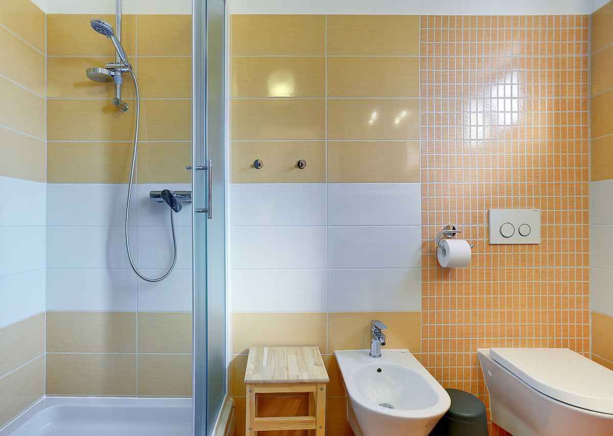 A bathroom with a shower, bidet, toilet, and a small wooden stool.
