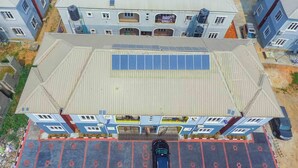 Un immeuble à plusieurs étages, doté d’un toit plat, de panneaux solaires et d’un espace de stationnement où se trouve une voiture.