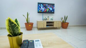 Un salon avec un téléviseur fixé au mur, un meuble en bois et deux plantes en pot.