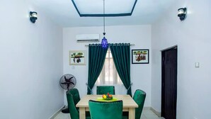 Une salle à manger avec une table et des chaises, un climatiseur, un ventilateur de plafond et une porte.