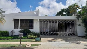 A modern white building with a large garage door, surrounded by well-maintained landscaping including palm trees and shrubs. - San Juan, 2 rooms w/private pool, outdoor kitchen/BBQ & nearby & peaceful (San Juan)
