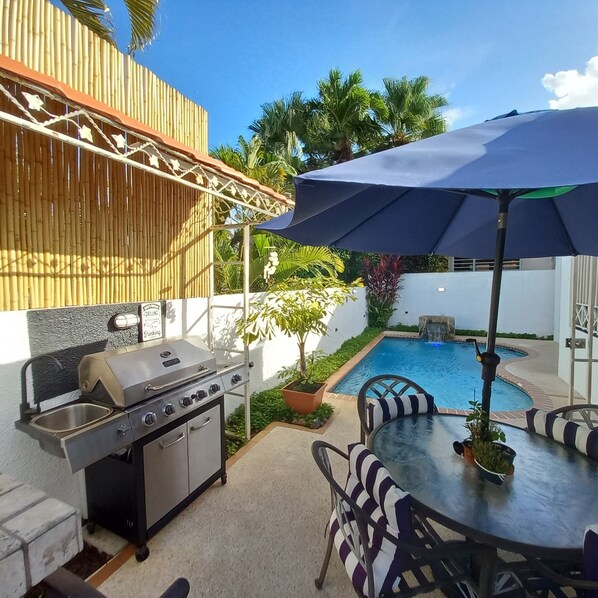 A patio with a grill, outdoor table, chairs, and a pool.