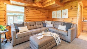 Un interior acogedor de cabaña de madera con un sofá modular, una mesa de centro y cuadros en las paredes.