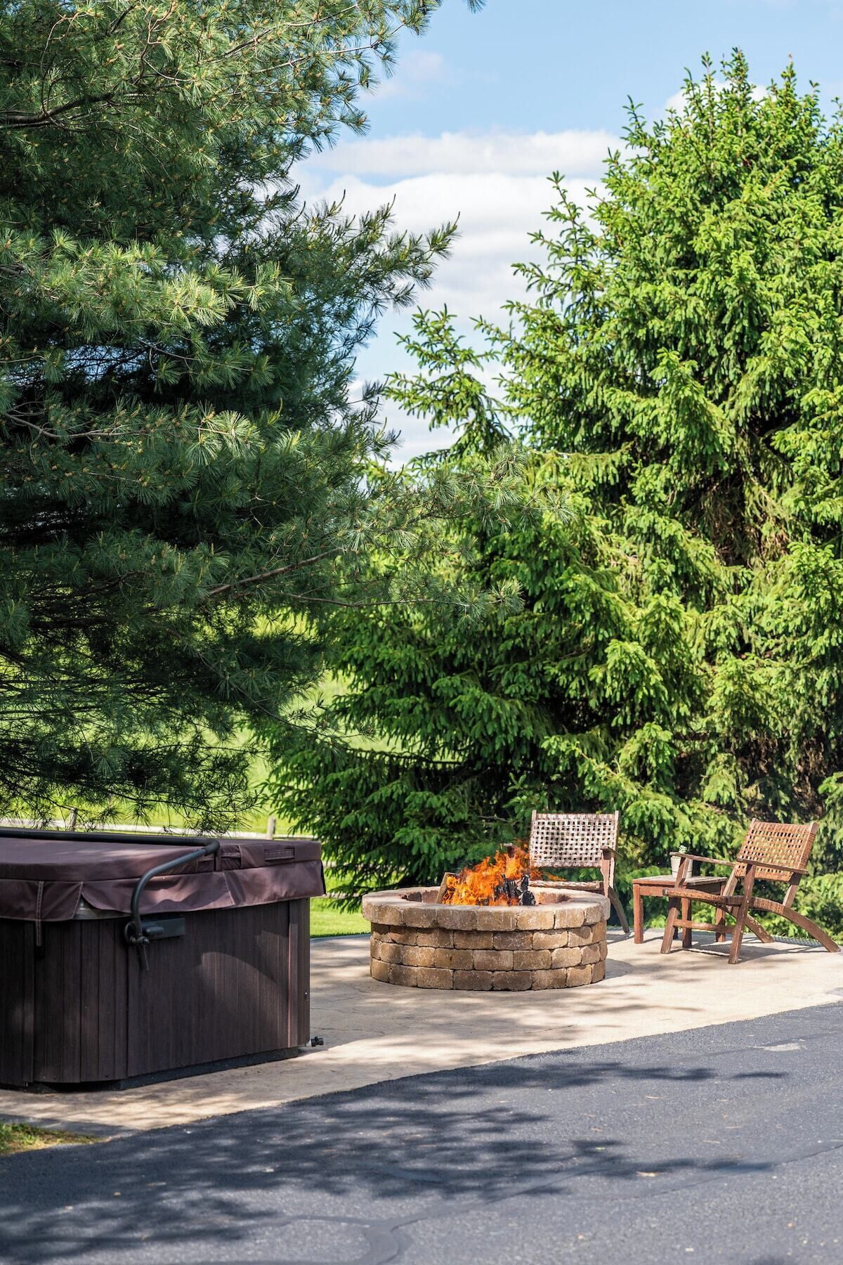 A covered hot tub, a stone fire pit, and two wooden chairs in a garden setting.