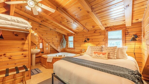 Dormitorio de cabaña de madera con cama, banca, bañera, ventilador de techo y ventana.