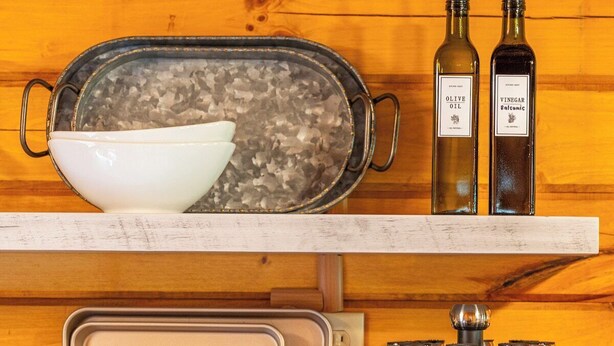 Una cocina con una olla en la estufa, dos botellas de aceite de oliva y vinagre, y especias en un escurridor.