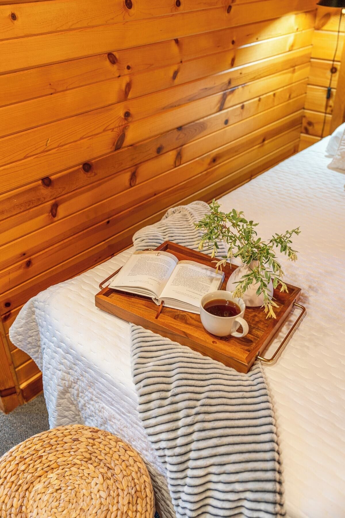 Een houten blokhut van binnen met een bed, een dienblad met een boek, een kop thee en een plant.