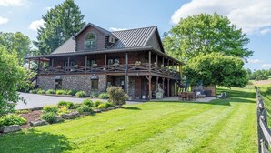 A large log cabin with a stone foundation, a covered porch, and a well-maintained lawn. - Spacious 6BR Retreat in Amish Country (Millersburg)