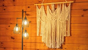 A room with a wooden wall, a white armchair with a patterned cushion, and a macrame wall hanging. - Spacious 6BR Retreat in Amish Country (Millersburg)