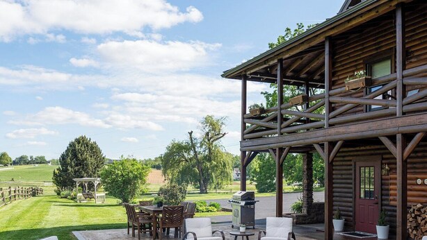 A covered outdoor patio with seating, a fire pit, and a view of a grassy field and trees. - Spacious 6BR Retreat in Amish Country (Millersburg)