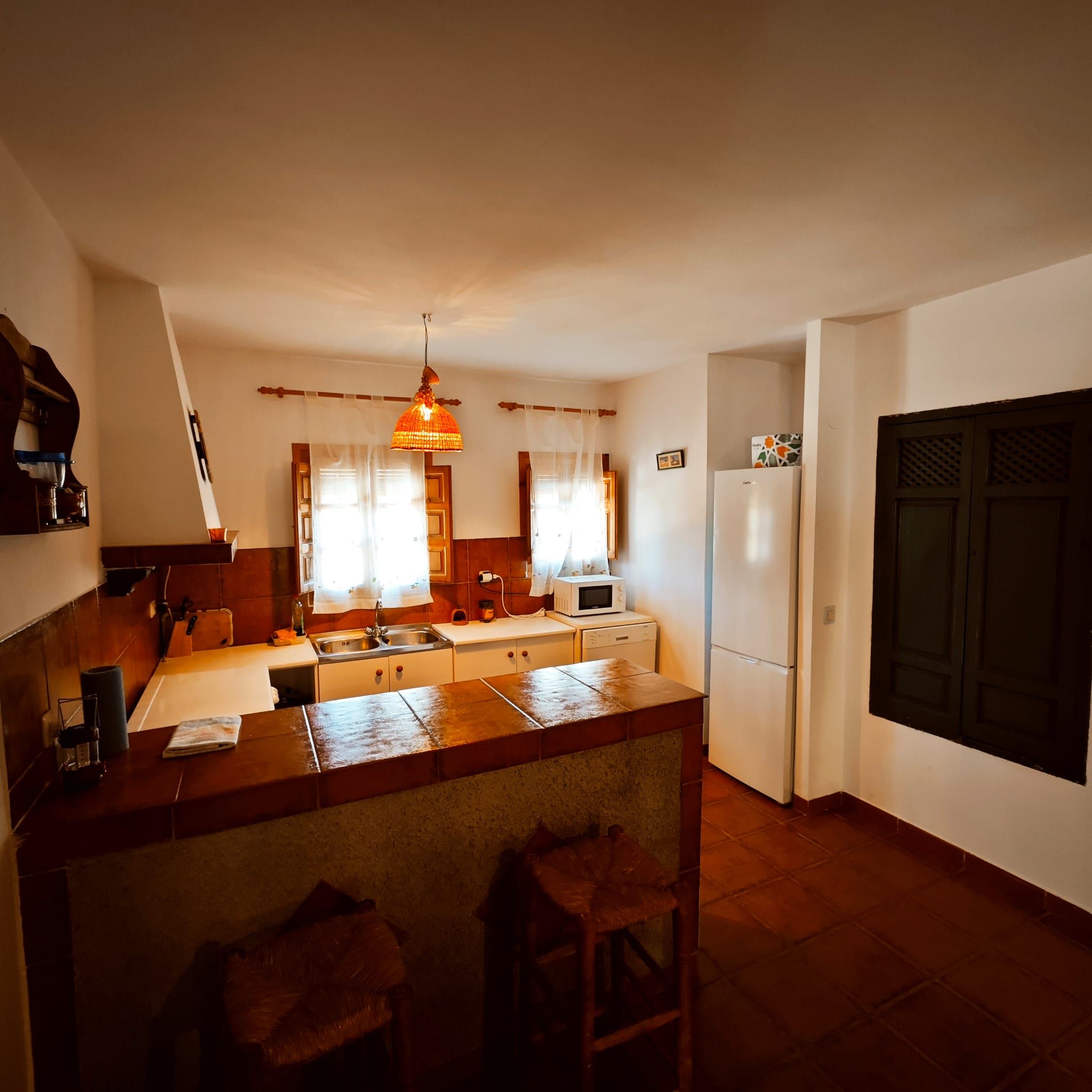A compact kitchen with a central island, a microwave, a refrigerator, and a hanging pendant light.