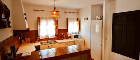 A compact kitchen with a central island, a microwave, a refrigerator, and a hanging pendant light.