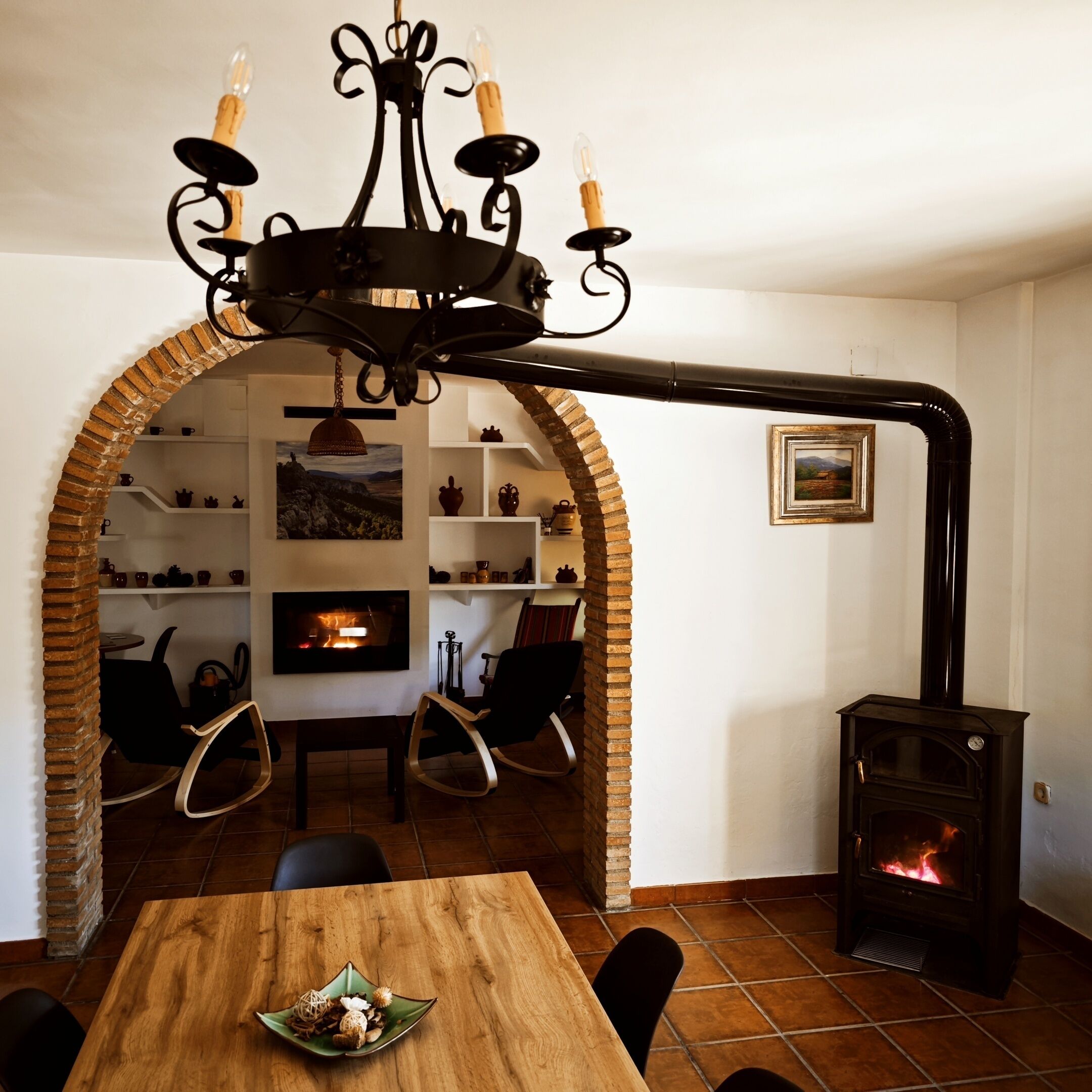 Een gezellige woonkamer met een open haard, een eettafel en een bakstenen boog die leidt naar een keuken.