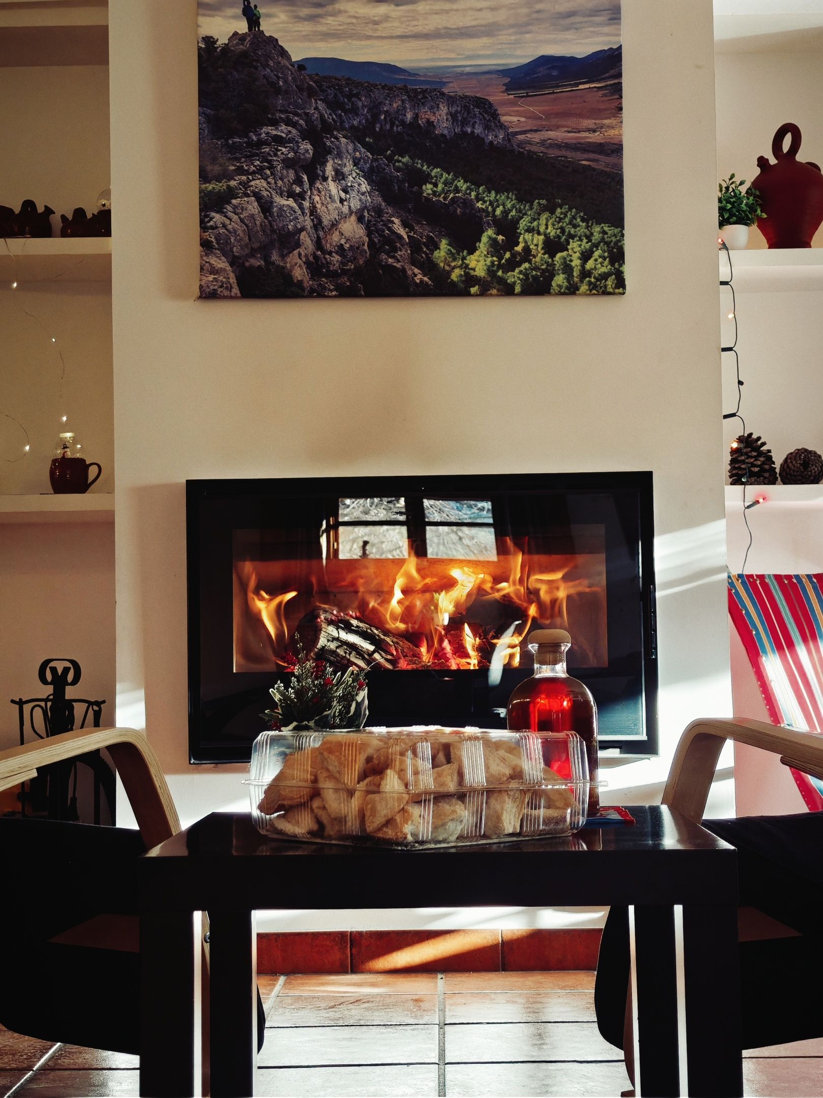 A living room with a fireplace, a flat-screen TV, and a painting of a mountainous landscape.