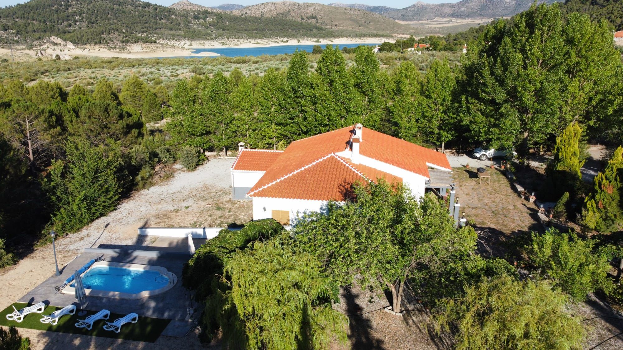 A villa with a swimming pool, surrounded by trees and a view of a lake and mountains.