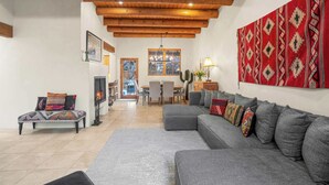 A spacious living room with a gray sectional sofa, a wooden ceiling, and a red patterned wall hanging.