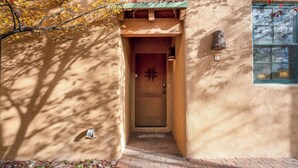 A building entrance with a wooden door, a small window, and a wall-mounted light fixture.