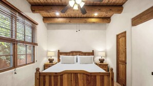 A bedroom with a wooden bed, two bedside lamps, a ceiling fan, and a large window with blinds.