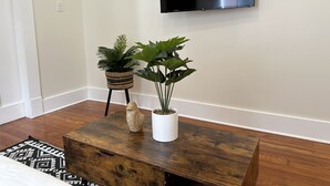 A room with a wooden coffee table, two potted plants, a decorative ceramic piece, and a mounted flat-screen TV on the wall.