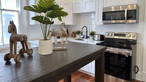 A modern kitchen with white cabinets, stainless steel appliances, a dark wooden table, decorative horse figurines, and a potted plant.