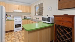A compact kitchen with wooden cabinets, a green countertop, a built-in oven, a microwave, and a wine rack. - "Klinger House" - Redcliffe Q 4020 (Redcliffe)