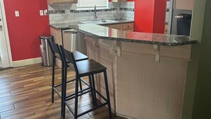 Una cocina con pared roja, armarios de madera, encimera de granito y pileta de acero inoxidable.