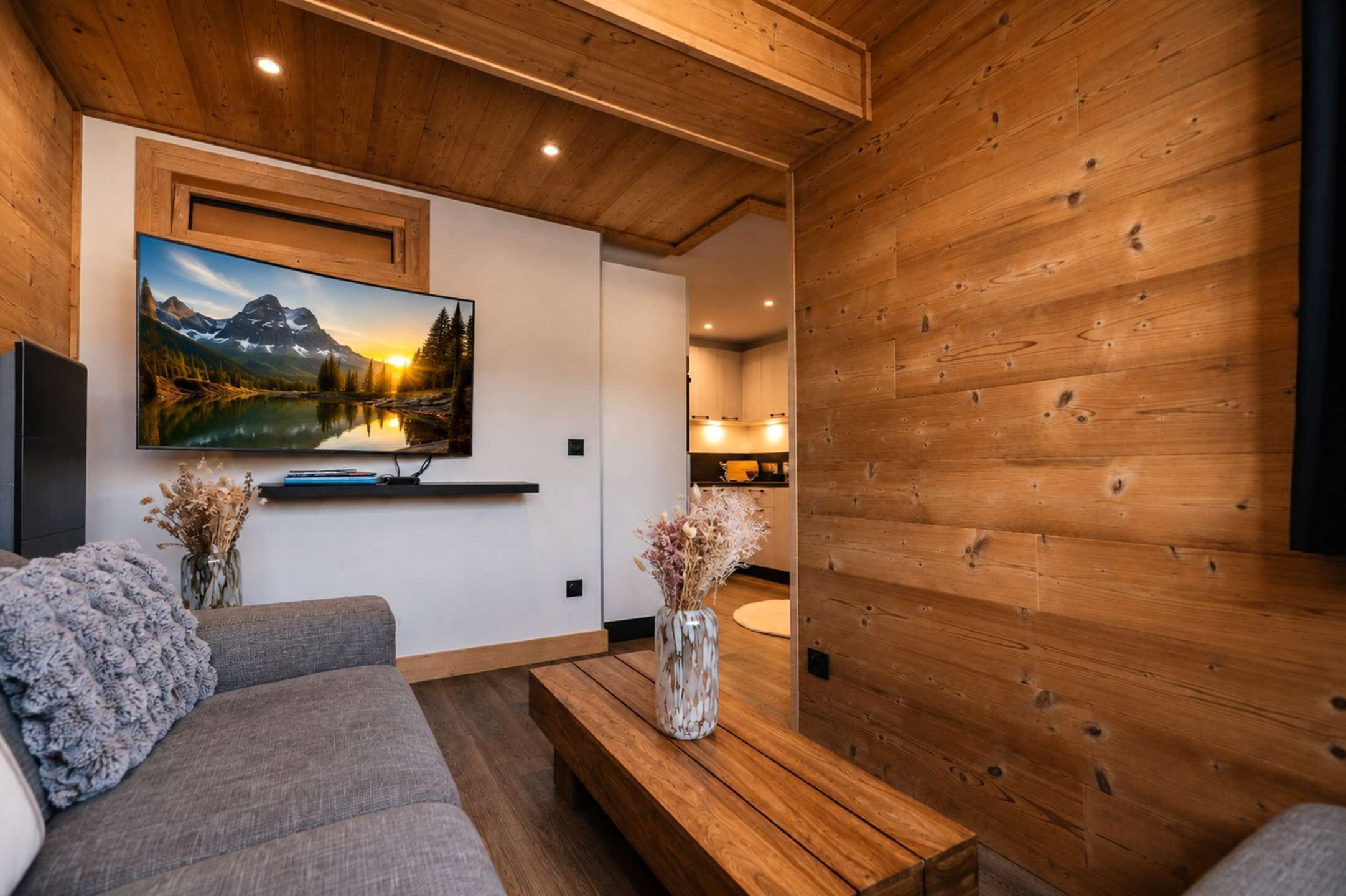 A modern living room with a flat-screen TV, a sofa, a coffee table, and a vase with dried flowers.