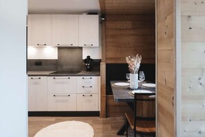A modern kitchen with white cabinets, a black countertop, and a dining area with a table set for two. - apartment for 4 people, very cozy and functional, renovated, mountain view, south facing,... (VAL THORENS)