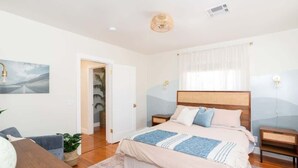 Ein Schlafzimmer mit einem großen Bett, Nachttischen, einem Holzkopfstück, einer Wandlampe und einer Tür zu einem anderen Raum.