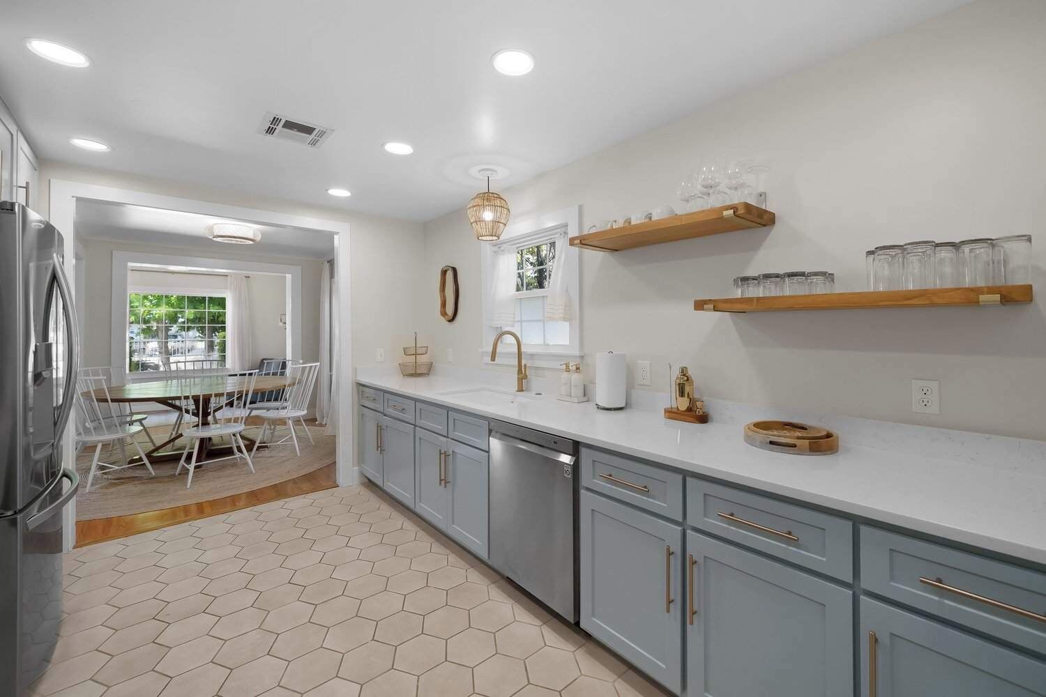 Uma cozinha moderna com armários cinza, uma geladeira de aço inoxidável e um espaço de refeições com mesa e cadeiras.