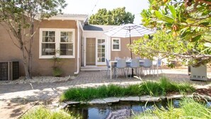 Ein Haus mit einer Terrasse, einem kleinen Teich und Sitzgelegenheiten im Freien.