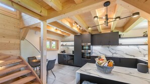 Una cocina moderna con encimeras de mármol, horno empotrado y zona de comedor con escalera de madera.