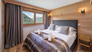 Un dormitorio con una cama grande, paredes de paneles de madera, una ventana con vista a la montaña y una mesita de noche pequeña.