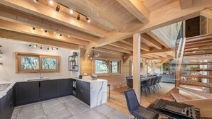 Una cocina moderna con una isla de mármol, vigas de madera y ventanas amplias.
