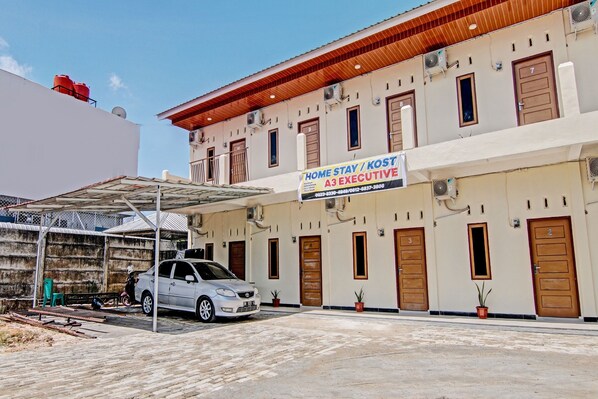 A building with multiple doors, a sign for 'Home Stay / Kost A3 Executive', and a parked car.