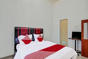 A hotel room with a bed, a TV on a stand, and a door.