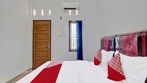 A hotel room with a bed, a window with blue curtains, an air conditioning unit, and a wooden door. - OYO 92135 A3 Homestay Syariah Executive (Pekanbaru)