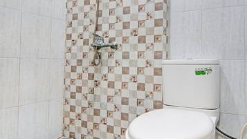 Une salle de bain avec un carrelage à motifs géométriques, une douche avec un mur décoré et des toilettes ornées d’un autocollant vert.