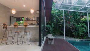 Eine moderne Küche mit Barhocker, einem großen Fenster und einem durch Glas geschützten Außenbereich mit Pflanzen und einem Pool.