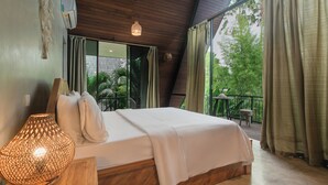 A bedroom with a bed, a bedside lamp, and a view of greenery outside. - Kalino Villa by Betterplace (Canggu)