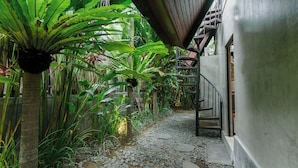A narrow pathway with a stone floor, surrounded by lush greenery and a metal staircase leading to a building. - Kalino Villa by Betterplace (Canggu)