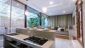 A modern kitchen with a gas stove, a dining area with a table set for two, and a living area with a sofa and decorative pillows. - Kalino Villa by Betterplace (Canggu)