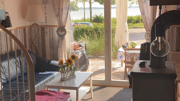 Ein gemütliches Wohnzimmer mit Holzbalkendecke, einer Couch, einem Couchtisch und Blick ins Freie durch Glasüren.