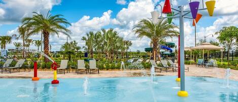 A swimming pool with water fountains, palm trees, and lounge chairs.