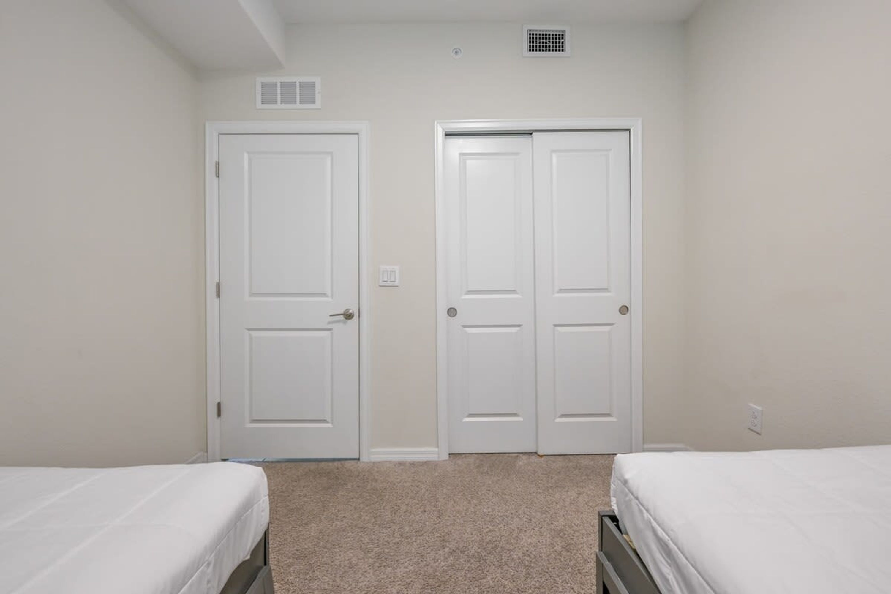 A bedroom with two white doors, a carpeted floor, and two beds.