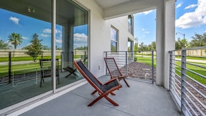 A balcony with two lounge chairs, a glass door leading to a patio, and a view of a green landscape.