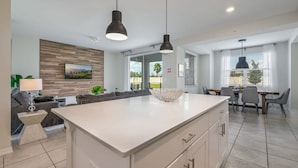 A modern kitchen with a central island, pendant lighting, and a dining area with a table and chairs.
