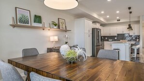 A modern kitchen with white cabinets, a central island, and a dining area with a wooden table and grey chairs.