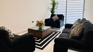 Ein modernes Wohnzimmer mit schwarzen Sofas, einem Glastisch und einem gemusterten Teppich.