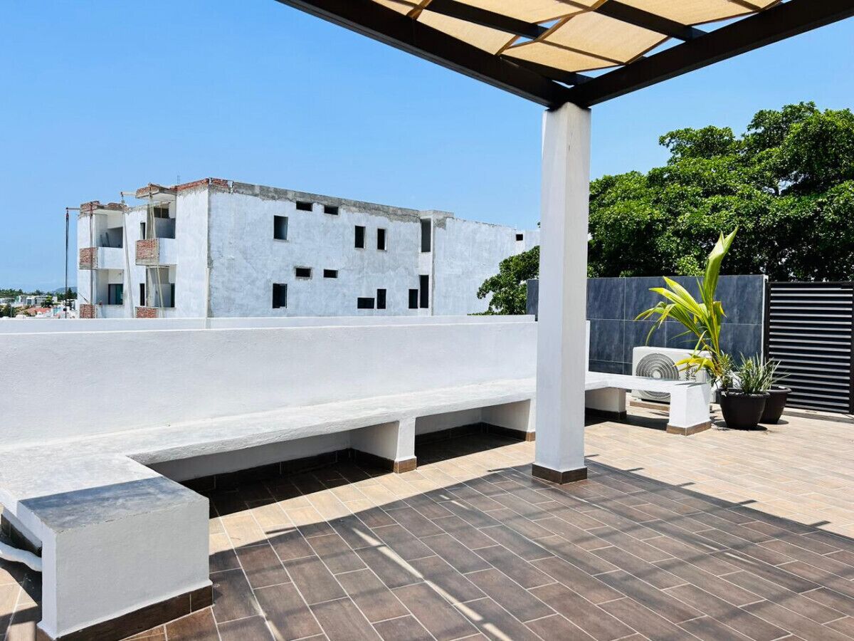 A rooftop terrace with a white bench, potted plants, and a view of a building in the background.